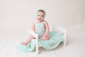 six month old baby sitting on a little bed